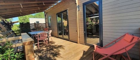 A wooden deck with a table and chairs, a red lounge chair, and a covered area with a pergola.