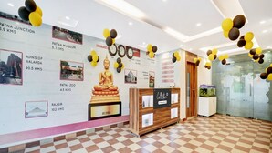 A reception area with a checkered floor, a Buddha statue, and informational posters on the wall. - Townhouse Jaganpura Crossway Patna (Patna)