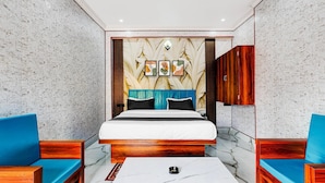 A bedroom with a bed, two blue chairs, a white coffee table, and a wall with a leaf pattern. - Townhouse Jaganpura Crossway Patna (Patna)