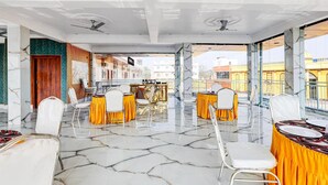 A spacious indoor area with marble flooring, white chairs, and tables set up for dining. - Townhouse Jaganpura Crossway Patna (Patna)