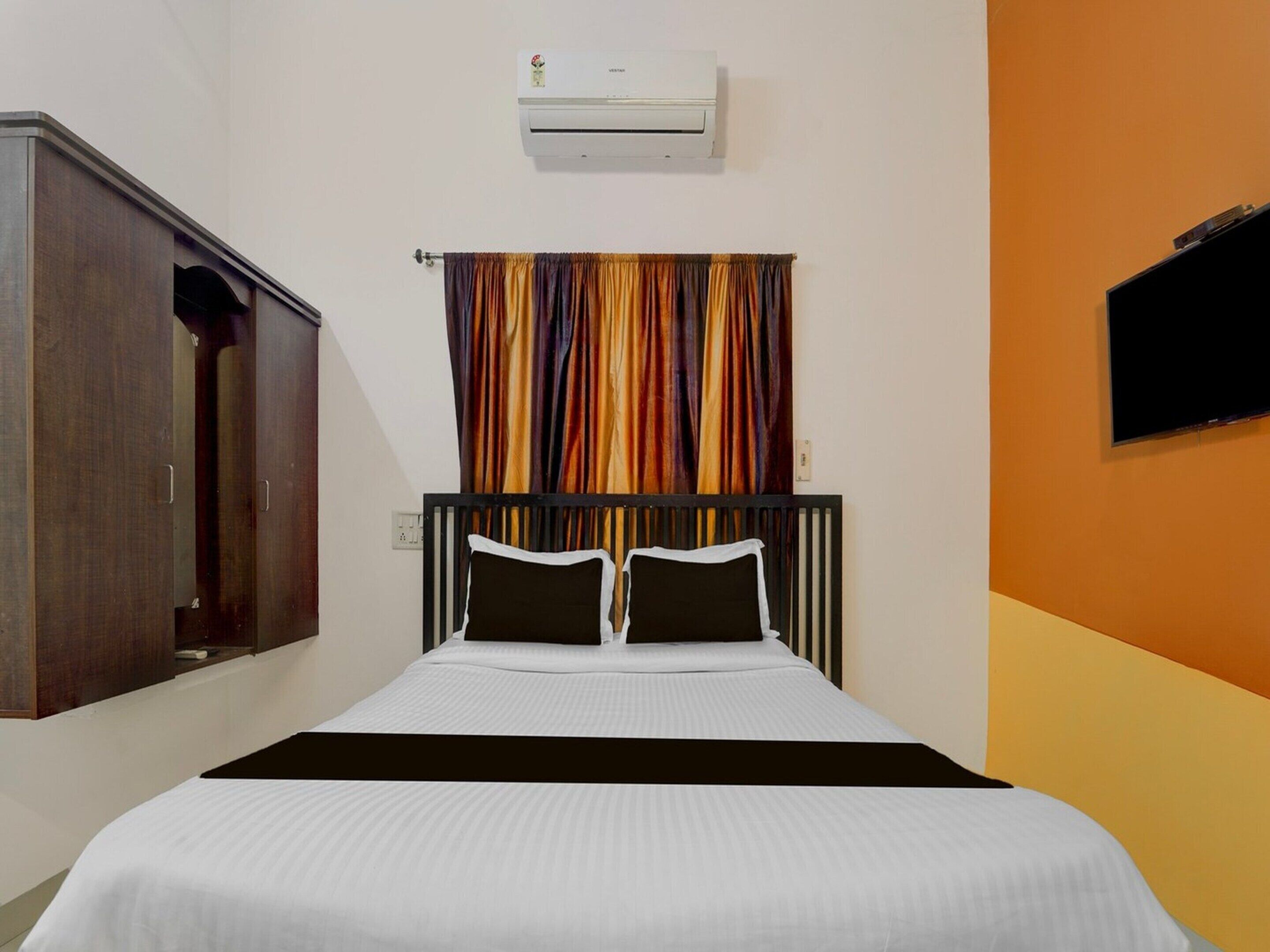 A hotel room with a bed, a wardrobe, an air conditioning unit, and a television.