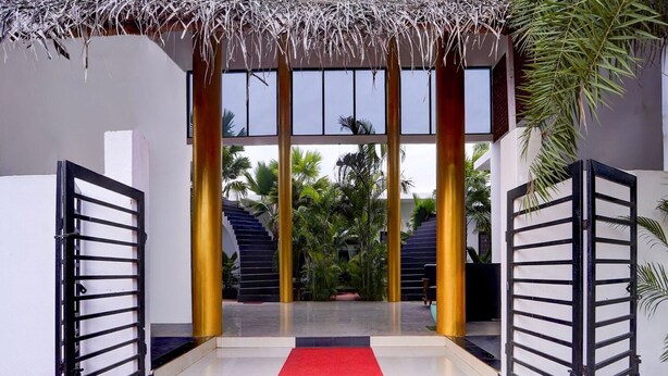 A hotel entrance with a red carpet, a thatched roof, and a staircase leading to a second floor. - Deluxe Vanam Resort (Vanur)