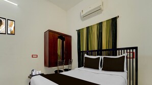 A hotel room with a bed, a wardrobe, a chair, a table with a kettle, and an air conditioning unit. - Deluxe Vanam Resort (Vanur)