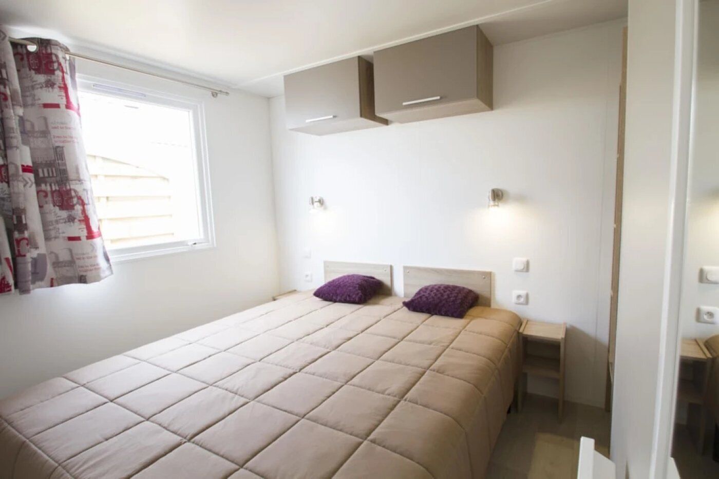 Ein Schlafzimmer mit einem Bett, zwei Nachttischen, einem Einbauschrank und einem Fenster mit Vorhängen.