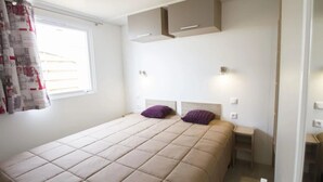 A bedroom with a bed, two nightstands, a built-in wardrobe, and a window with curtains. - Camping 4 étoiles - Parc aquatique - eeidfa (Valras-Plage)