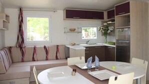 A compact kitchen with a dining area, a built-in oven, and a refrigerator. - Camping 4 étoiles - Parc aquatique - eeidfa (Valras-Plage)