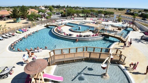 A large outdoor swimming pool with multiple sections, a wooden deck, and lounge chairs. - Camping 4 étoiles - Parc aquatique - eeidfa (Valras-Plage)