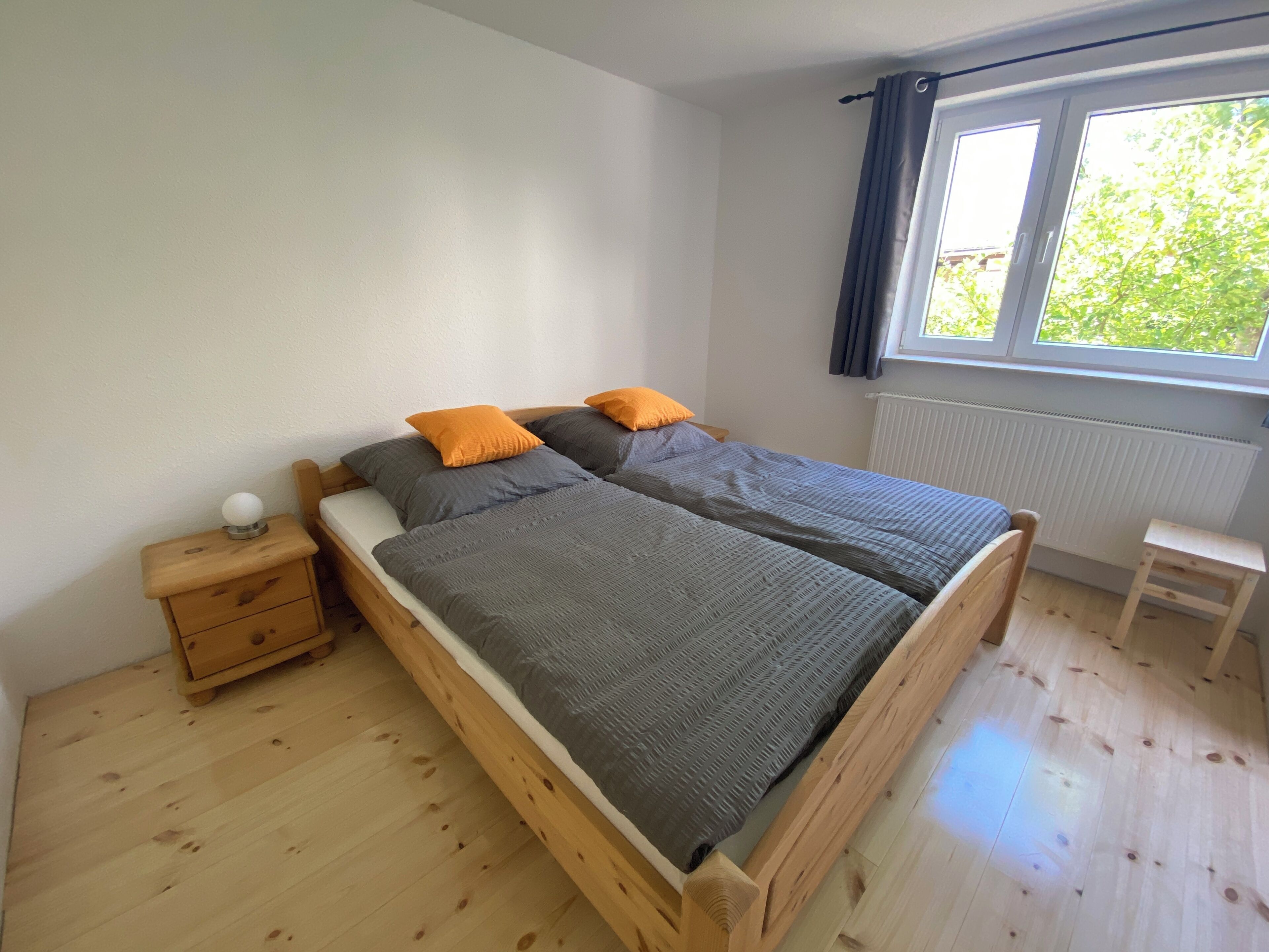 A bedroom with a wooden bed, a nightstand, a window with curtains, and a radiator.