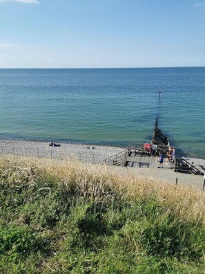A beach with a wooden pier extending into the water, a rocky shoreline, and grassy areas in the foreground.