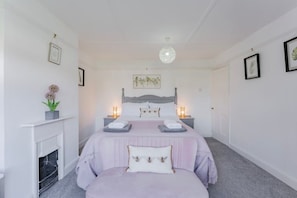 Ein Schlafzimmer mit einem Bett, Nachttischen, einer Pendelleuchte, einem Kamin und gerahmten Kunstwerken an den Wänden.