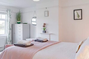 A bedroom with a bed, a dresser, a mirror, a shelf with a plant, and a framed picture on the wall.