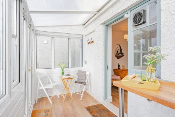 A room with a wooden floor, a small table with chairs, a window with a view, and a door leading to another room.