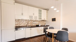 Een moderne keuken met witte kasten, een betegelde spatwand, en een eethoek met een ronde tafel en stoelen.