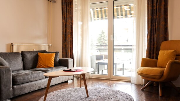 Een woonkamer met een bank, fauteuil en salontafel, een radiator en uitzicht door een glazen deur.