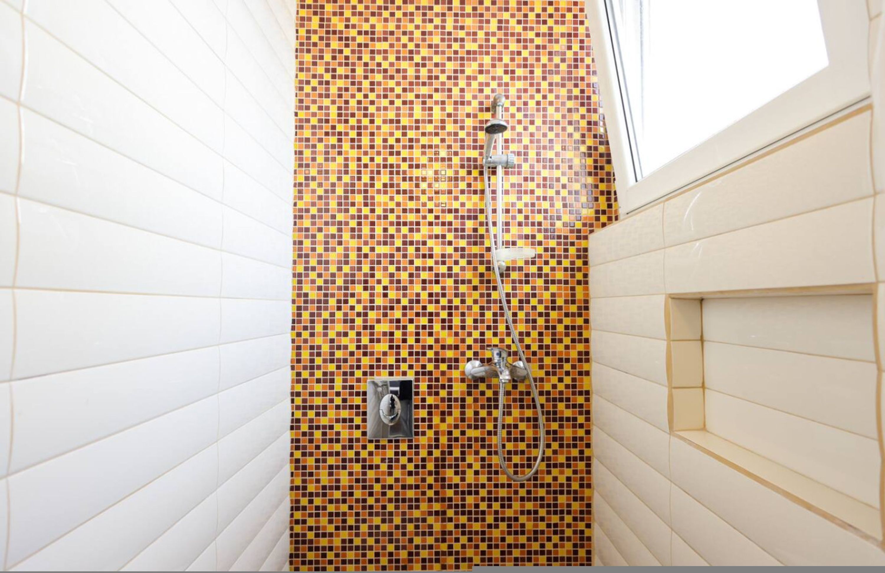 A bathroom with a tiled wall, a shower, and a window.