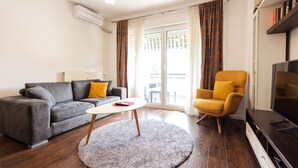 Een woonkamer met een bank, fauteuil, televisie en een kleine tafel.