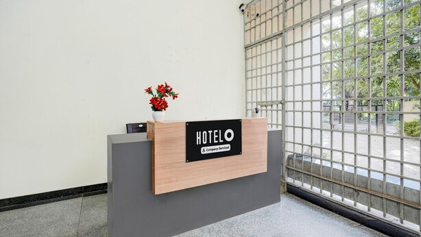 A reception desk with a 'HOTELO' sign, a potted plant, and a view through a metal gate. - Super Townhouse City Center Ernakulam (Kanayannur)