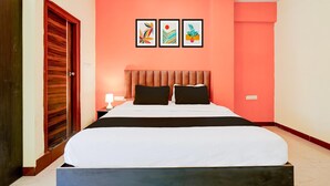 A bedroom with a bed, a wooden door, and three framed pictures on the wall. - Super Townhouse City Center Ernakulam (Kanayannur)