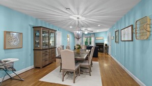 A dining room with a wooden table and chairs, a chandelier, and a cabinet with glass doors.