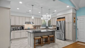 A modern kitchen with white cabinetry, a central island with stools, stainless steel appliances, and pendant lighting.