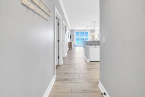 A hallway with a wooden floor, white walls, and a view of the ocean through large windows. - ☀️Gulf FRONT | Pools + Hot Tub | Beach Service | Emerald Isle 508☀️ (Panama City Beach)