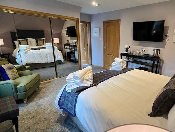 A hotel room with a bed, a sofa, a desk, a television, and a mirror. - Copper Beeches (Elgin)
