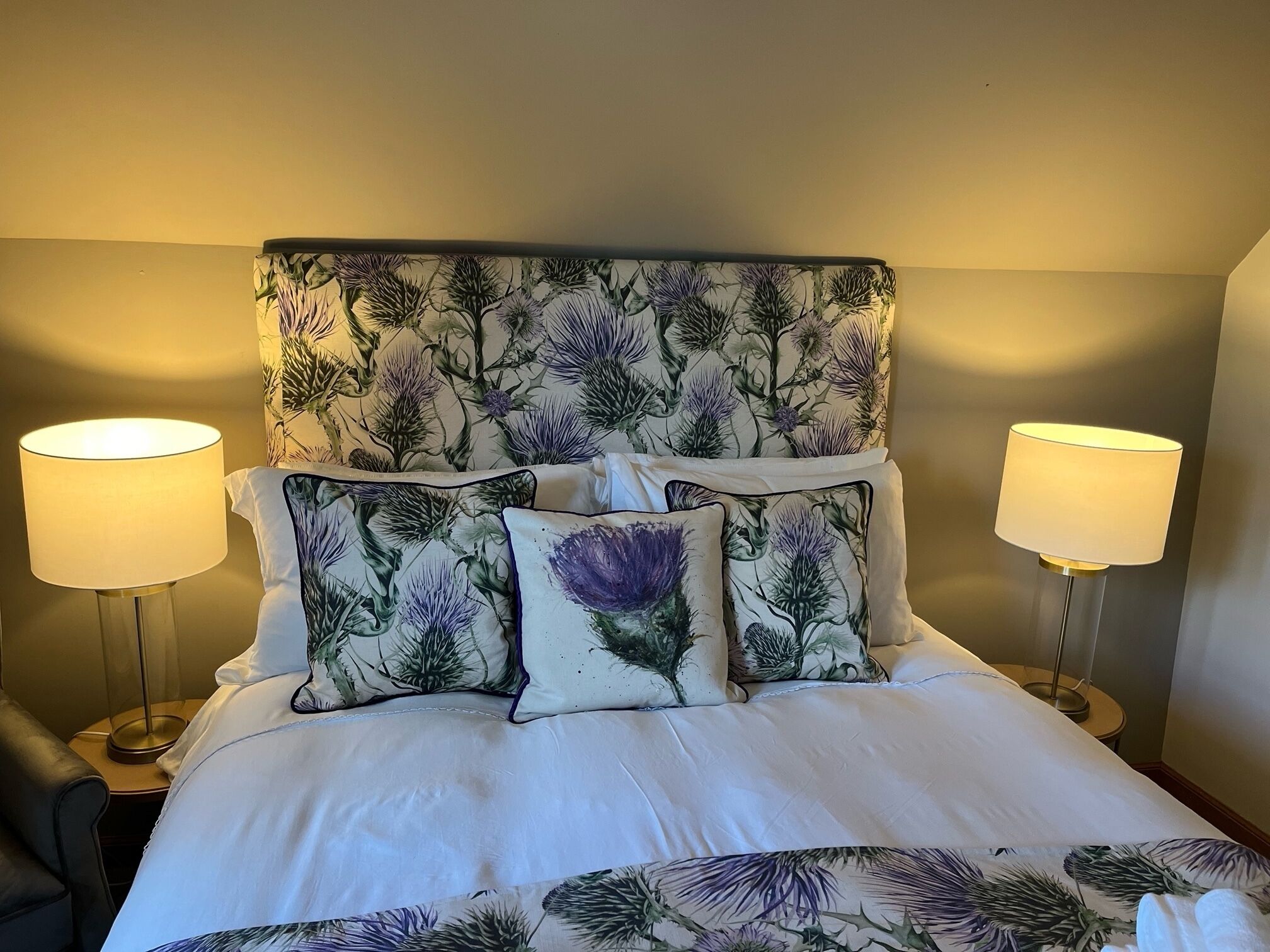Een bed met een bloemen hoofdbord, twee bedlampen en een witte sprei.