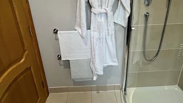 A bathroom with a glass shower enclosure, a white bathmat, and a white bath towel hanging on a hook.