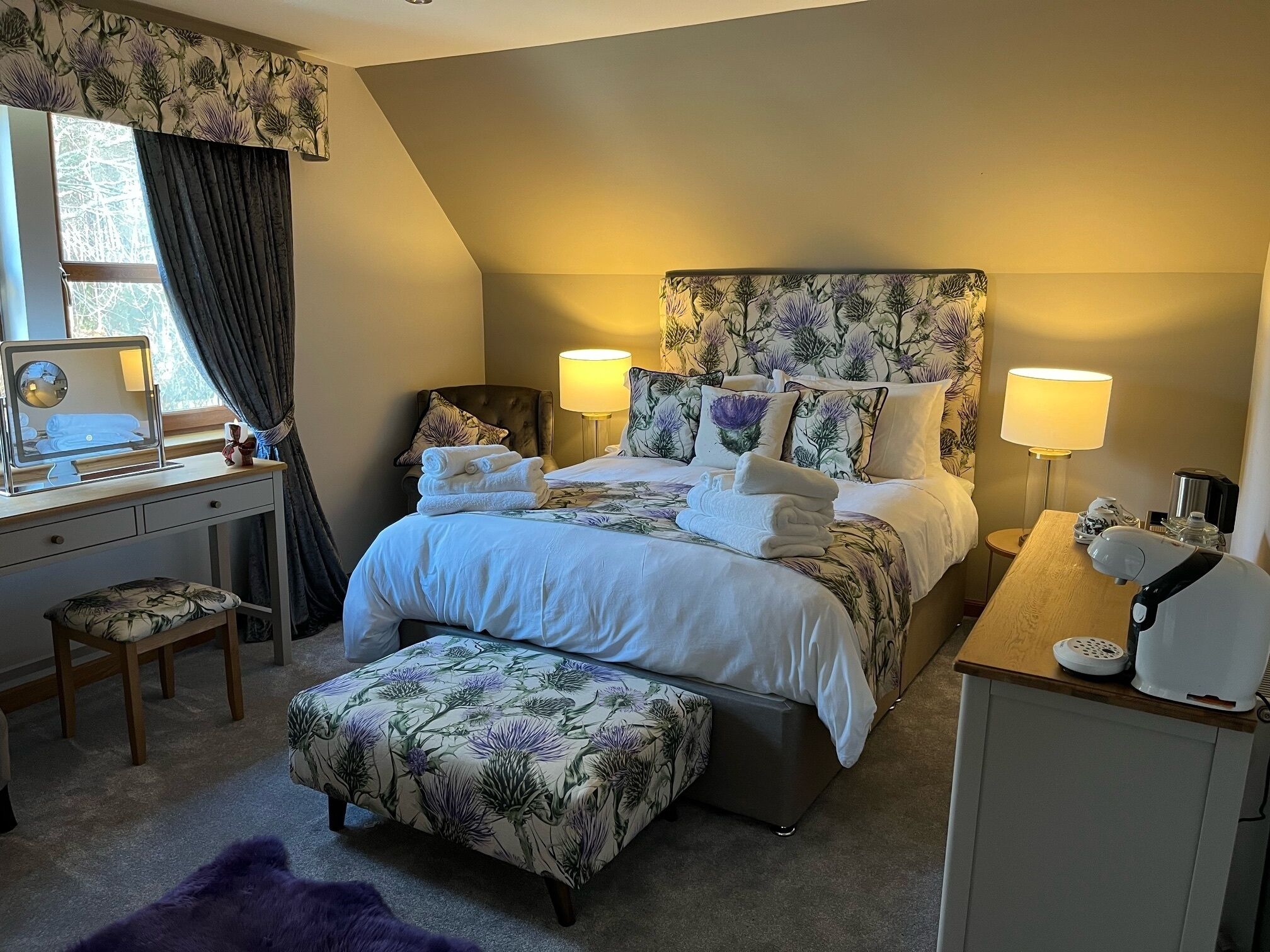 A bedroom with a bed, bedside tables, a desk, a chair, a mirror, and a window with curtains.