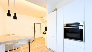 Een moderne keuken met witte kastjes, een ingebouwde oven en hangende lampen.