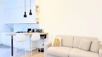 A modern kitchen with white cabinets, a dining area with two chairs, and a sofa with a cushion.