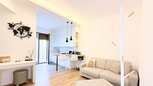 Een moderne woonkamer met een bank, een bureau en een keuken in de achtergrond.