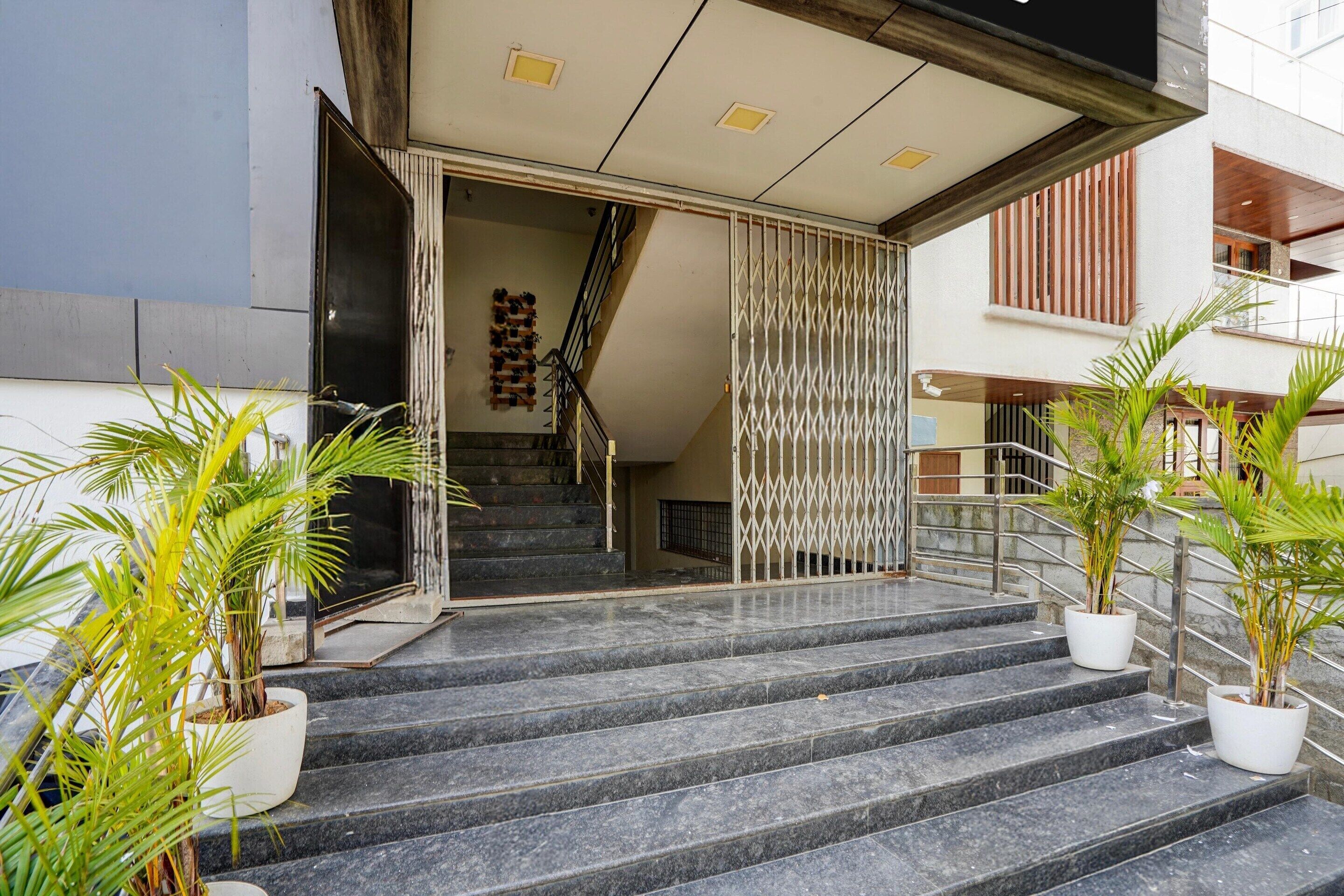 A staircase leading to a building entrance with a metal gate, potted plants, and a wooden staircase visible in the background.