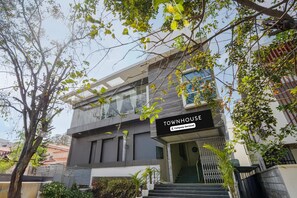 A modern townhouse with a sign indicating it is company-serviced, a staircase leading to the entrance, and a view of the surrounding area. - Townhouse Hospital Road (Bengaluru)