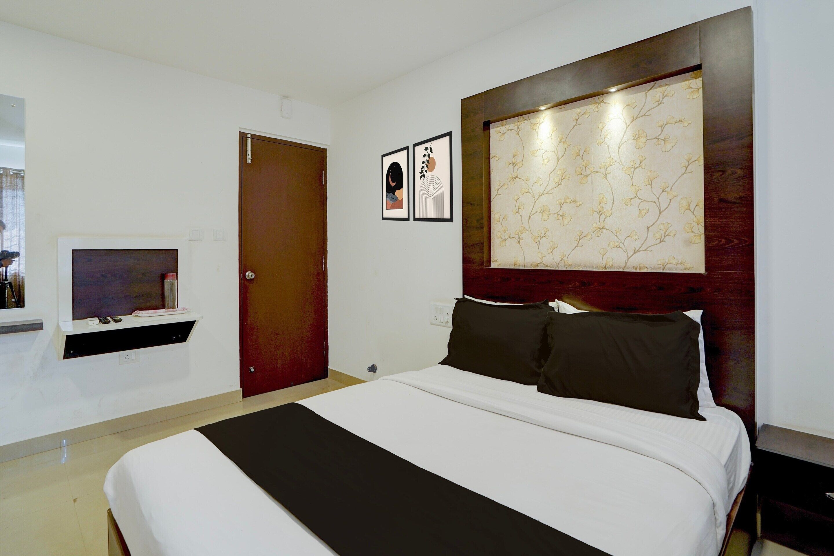 A hotel room with a bed, a TV, a door, and a wall-mounted artwork.