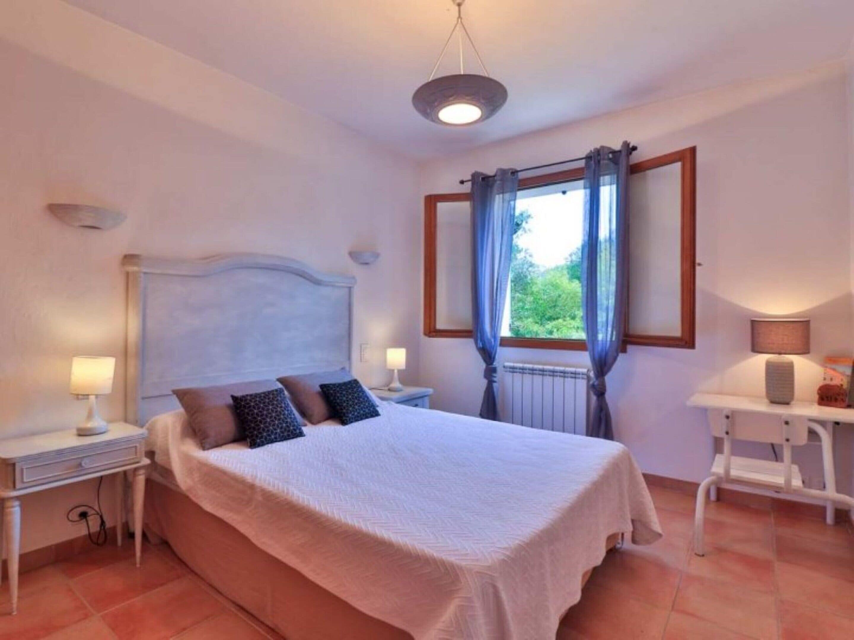 A bedroom with a bed, nightstands, a desk, and a window with curtains.