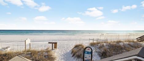 Una playa con un paseo de madera que llega hasta la orilla, un cartel de seguridad y una banca.