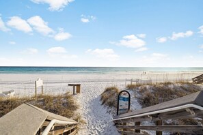 Ein Strand mit einer Holzpromenade, die zum Ufer führt, einem Sicherheitsschild und einer Bank.
