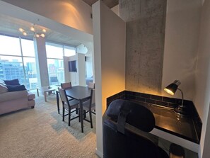 A modern living room with a sofa, dining table, and chairs, a kitchen area with a sink and countertop, and large windows offering a city view. - Glass House 21st Floor Condo with Amazing View (Denver)