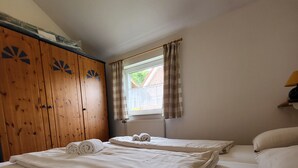 A room with two beds, wooden wardrobe, window with curtains, and a lamp on a bedside table. - Haus Teelke vacation home in an idyllic location directly on the river (Papenburg)
