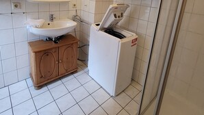 A bathroom with a sink, mirror, shower, and a laundry machine. - Haus Teelke vacation home in an idyllic location directly on the river (Papenburg)
