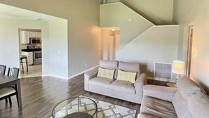 A modern living room with a sofa, a glass coffee table, and a staircase leading to an upper level. - 4BR Montego Bay Villa Near Disney (Kissimmee)