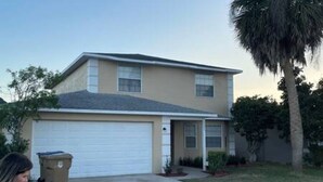 A two-story residential building with a garage, a small front porch, and a palm tree in the yard. - 4BR Montego Bay Villa Near Disney (Kissimmee)