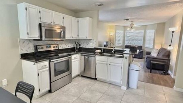 A compact kitchen with white cabinets, a microwave, stove, and dishwasher. - 4BR Montego Bay Villa Near Disney (Kissimmee)