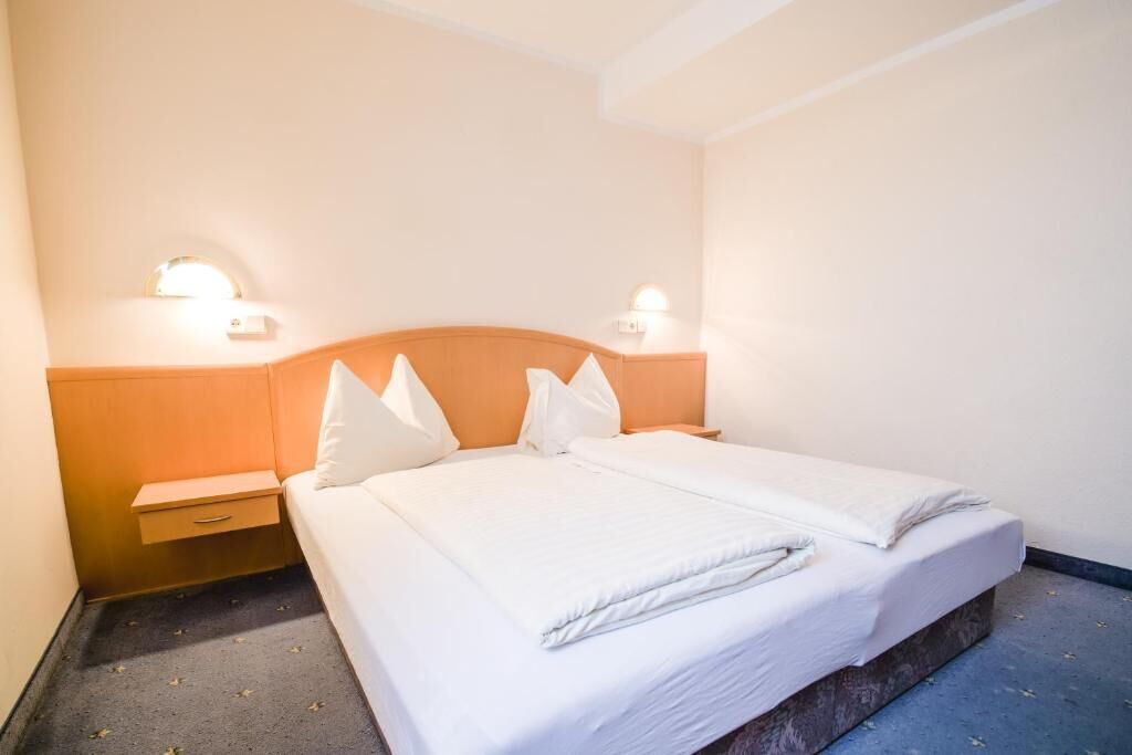 A hotel room with a bed, bedside tables, and wall-mounted lights.