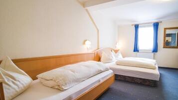 Una camera d'albergo con due letti singoli, una finestra con tende blu, uno specchio e un punto luce a parete.