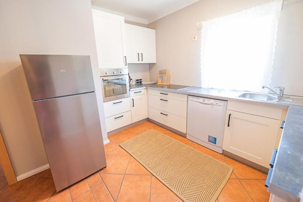 Een moderne keuken met witte kasten, roestvrijstalen apparatuur en een vloerkleed met een herringbone-patroon.