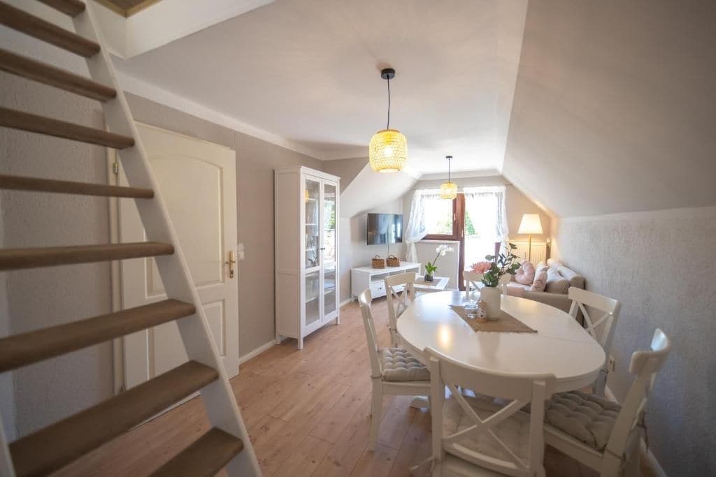 Ein Essbereich mit einem weißen Tisch und Stühlen, einer Treppe und einer Tür zu einem weiteren Raum.