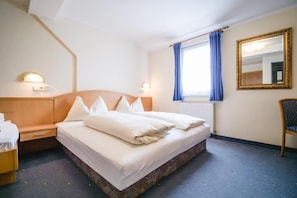 A hotel room with a bed, bedside tables, a window with curtains, a radiator, and a mirror on the wall. - Landhaus Gretl (Krumpendorf am Woerther See)