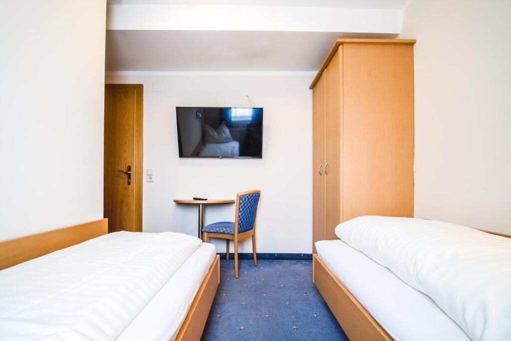 Ein Hotelzimmer mit zwei Betten, einem Fernseher an der Wand, einem Schreibtisch und einem Stuhl.
